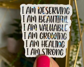 May include: A white sticker with iridescent glitter features the text "I am deserving, I am beautiful, I am valuable, I am growing, I am healing, I am strong".