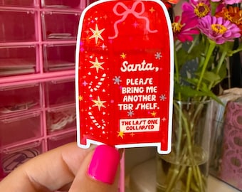May include: A red sticker in the shape of a gift box with the text "Santa, PLEASE BRING ME ANOTHER TBR SHELF. THE LAST ONE COLLAPSED." The sticker has a bow, stars, and candy cane designs.
