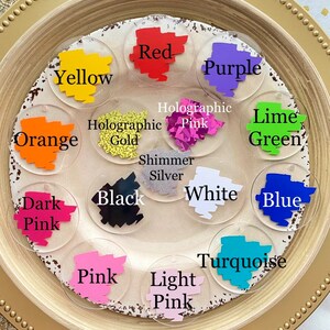 Peut inclure: Un ensemble de 14 pastilles de peinture acrylique rondes de diff&eacute;rentes couleurs et finitions, notamment rouge, violet, jaune, orange, vert lime, bleu, turquoise, rose, rose clair, rose fonc&eacute;, noir, blanc, or holographique et rose holographique. Les pastilles sont dispos&eacute;es en cercle sur une assiette dor&eacute;e.
