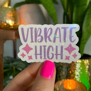 May include: A white sticker with iridescent glitter and purple lettering that reads "VIBRATE HIGH" with pink stars on either side.