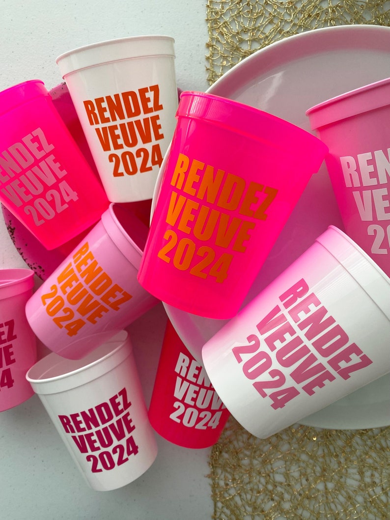 Peut inclure: Un ensemble de gobelets en plastique rose et blanc avec le texte "Rendez Vous 2024" imprim&eacute; dessus. Les gobelets sont dispos&eacute;s en pile, certains se chevauchant.