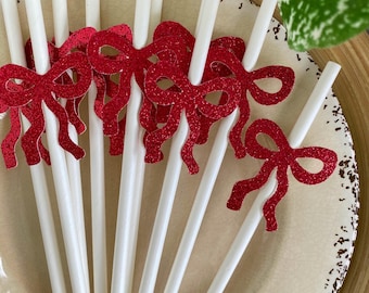 May include: White plastic straws with red glitter bow accents arranged on a decorative plate. The bows are a bright red color and add a festive touch to the straws. The plate is off-white with a brown rim.