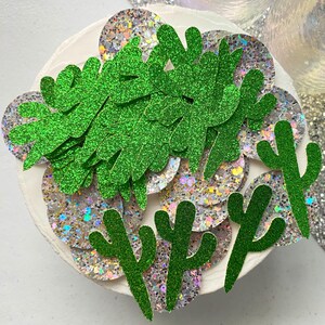 May include: Green glitter cactus and leaf shapes on a white background with iridescent glitter circles.