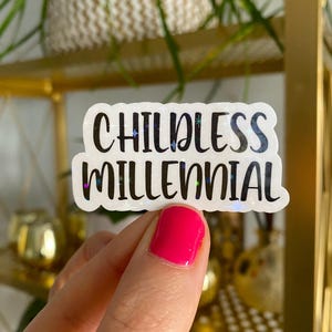 May include: A white sticker with a glittery finish and black text that reads "Childless Millennial".