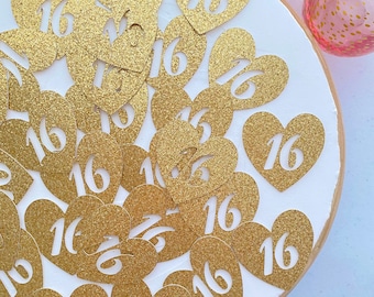 May include: A white plate with gold glitter heart-shaped confetti with the number 16 printed on each. The confetti is scattered on the plate.