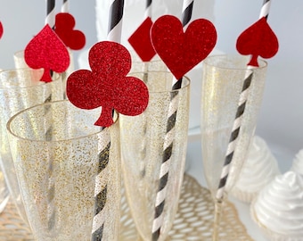 May include: Gold glitter champagne flutes with black and white striped straws and red glitter card suit toppers. The suits are hearts, clubs, spades, and diamonds.