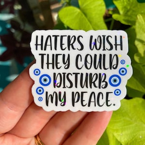 May include: White sticker with the text "Haters wish they could disturb my peace."  The text is in black and surrounded by blue evil eye charms.