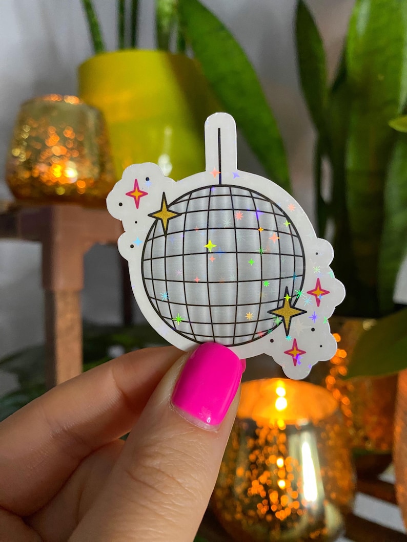 Op de afbeelding: Een witte sticker met een zilveren glitter discobal en kleurrijke sterren. De sticker is op een witte achtergrond.