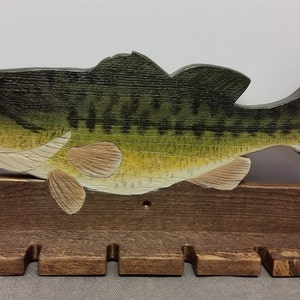 Peut inclure: Un porte-cannes en bois avec un poisson de pêche en bois sculpté sur le dessus. Le porte-cannes a six emplacements pour les cannes et est teinté d'une couleur brun foncé.