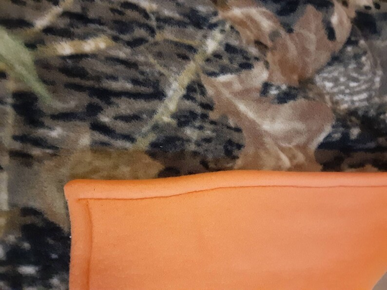 May include: A camouflage fleece blanket with a bright orange fleece lining. The blanket is soft and warm, ideal for keeping you cosy on cold days.