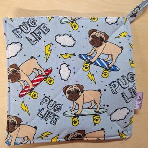 May include: Square light blue potholder with a repeating pattern of pugs on skateboards, clouds, and lightning bolts. The words "Pug Life" are printed on the potholder. A small loop is attached to one corner.