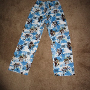 May include: Blue pajama pants with a white background and a repeating pattern of characters from the Star Wars Clone Wars series. The text "Clone Wars" is repeated throughout the pattern.