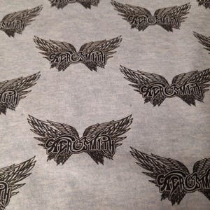 May include: Pale grey fabric with a repeating pattern of black Aerosmith logos featuring stylized wings. The band's name is written in a decorative font within the wings.