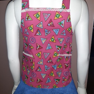 May include: Pink and blue Girl Scout apron with a white lace trim. The apron has a pattern of colorful triangles with Girl Scout badges and symbols. The apron has two pockets.