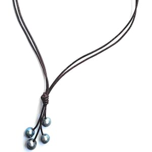 May include: A brown leather necklace with a single pearl at the top and three pearls at the bottom.