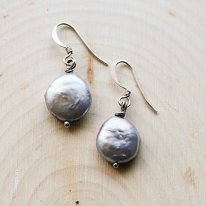 May include: A pair of silver earrings with a round, light gray pearl on each earring.