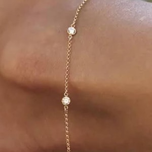 Puede incluir: Un delicado tobillo de cadena de oro con pequeñas piedras transparentes. El tobillo está hecho de una cadena fina y tiene un diseño simple.