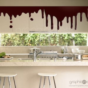 May include: A kitchen with white cabinets and a brown chocolate-like design on the top of the cabinets. The kitchen has a window with green trees outside, a stainless steel sink, and a hob.