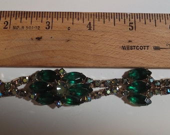 May include: A vintage green and silver rhinestone bracelet with a clasp closure. The bracelet is made of metal and features a row of emerald green rhinestones.
