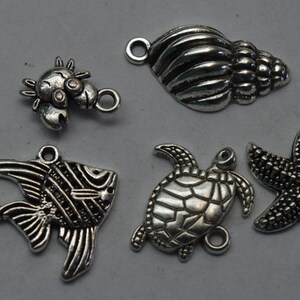 May include: A set of six silver-toned metal charms featuring various sea creatures and a seashell. The charms include a seahorse, a fish, a turtle, a starfish, a crab, and a seashell.