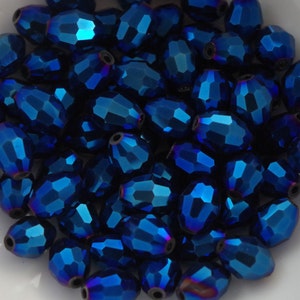 May include: A close-up of a pile of iridescent blue faceted glass beads. The beads are oval shaped and have a metallic sheen.