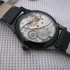 May include: A black wristwatch with a black leather band and a clear case revealing the inner workings of the watch. The watch face is visible and has the text "3311514" printed on it.