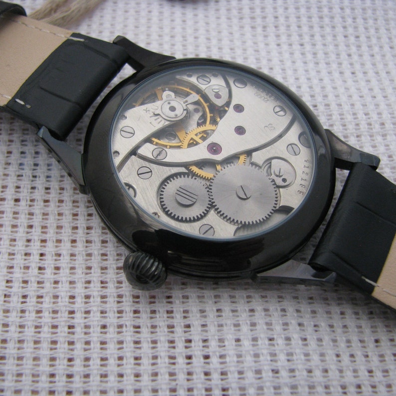 May include: A black wristwatch with a black leather band and a clear case revealing the inner workings of the watch. The watch face is visible and has the text "3311514" printed on it.