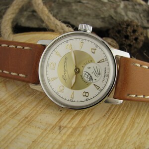 Puede incluir: Un reloj de pulsera plateado con una esfera blanca y detalles dorados. El reloj tiene una correa de cuero marr&oacute;n con costuras blancas. La esfera del reloj tiene las palabras "СССР" y "ЧaconoB" impresas.