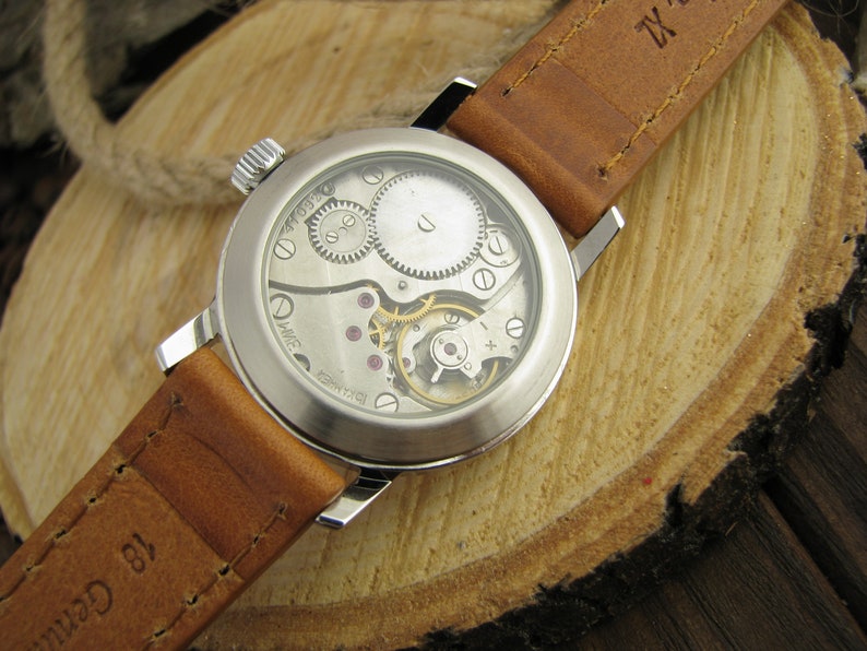 Puede incluir: Un reloj de pulsera plateado con una correa de cuero marr&oacute;n. El reloj tiene una parte posterior transparente que revela el funcionamiento interno del reloj.