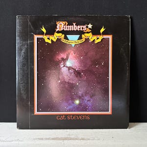 Puede incluir: Portada de álbum vintage de "Numbers" de Cat Stevens. La portada presenta una imagen vibrante de nebulosa en tonos morados, rosas y verdes. El título del álbum está en una fuente decorativa con una estrella, y el nombre del artista está en la parte inferior.