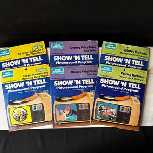 Könnte beinhalten: Eine Sammlung von Vintage "Show 'N Tell" Plattenspielern und dazugehörigen Geschichtenbüchern. Die Bücher tragen Titel wie "Big Bird in Goldilocks & The Three Bears" und Disney-Cartoons. Die Plattenspieler sind beige.