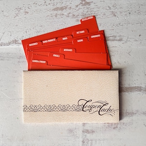 May include: A beige textured coupon organizer with the text Coupon Cache and a decorative border. Inside are bright red tabbed dividers labeled with categories including Canned & Frozen, Cereals, Beverages, Baking, Condiments, Pet Foods, Drugs, Paper Products, and Household.
