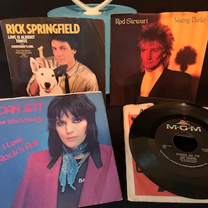 May include: A collection of four vintage music records and singles. The records include Rick Springfield's "Love is Alright Tonite", Joan Jett and the Blackhearts' "I Love Rock 'n' Roll", Rod Stewart's "Young Turks", and a 45 RPM record by Kim Carnes titled "Someone Like You".