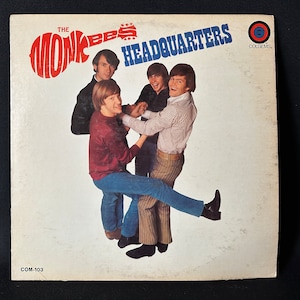 Puede incluir: Una portada de disco de vinilo vintage con una banda llamada "The Monkees" con el título del álbum "Headquarters" y la discográfica "Colgems". La portada presenta una foto de los miembros de la banda en una pose divertida.