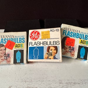May include: Three boxes of flashbulbs, two are blue and white with the brand name "SYLVANIA BLUE DOT FLASHBULBS" and the other is blue and white with the brand name "GE FLASHBULBS". All three boxes have a red price tag sticker on them.