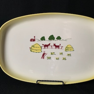 Könnte beinhalten: Eine weiße ovale Servierplatte mit gelbem Rand. Die Platte zeigt eine handgemalte Szene einer Farm mit einem roten Stall, Heuballen, Bäumen und zwei braunen Pferden.