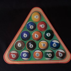 Può includere: Un triangolo di feltro verde con 15 palle da biliardo numerate da 1 a 15. Le palle sono disposte a forma di piramide, con la palla 1 in cima e la palla 15 in fondo.