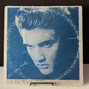 Peut inclure: Une pochette d'album de disque vinyle bleu et blanc avec un portrait rapproché d'Elvis Presley. Le titre de l'album est "Special Record" et le texte "Selections from the 8-record 25th Anniversary Album" est imprimé sous le portrait. La pochette est légèrement usée et décolorée.