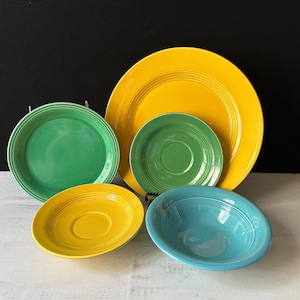 Puede incluir: Un juego de cuatro platos de cerámica en amarillo, verde y azul. Los platos son todos redondos y tienen un diseño sencillo.