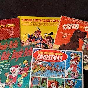 May include: A collection of vintage children's vinyl records with colorful covers featuring illustrations of Santa Claus, a sleigh, a cat and dog, and a group of children. The titles include "Children's Stories in Song and Verse", "Sleigh Ride/Jingle Bells", "Treasure Chest of Kiddie's Songs", "'Twas the Night Before Christmas", and "Cats and Dogs".