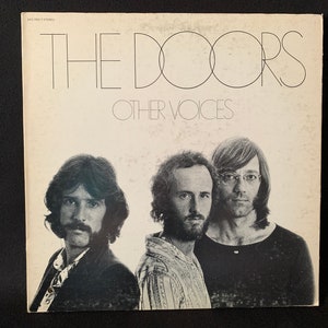 May include: A black and white album cover for The Doors album "Other Voices". The cover features a photo of the band members: Ray Manzarek, Robby Krieger, and John Densmore.
