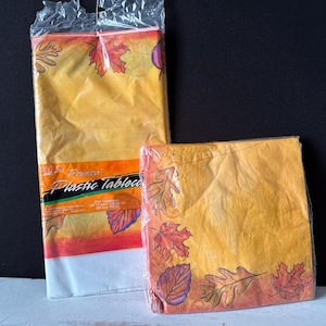 May include: Two packages of fall-themed plastic tablecloths. The larger tablecloth is yellow with orange, red, and brown leaves and the smaller tablecloth is yellow with orange, red, and brown leaves and a red border.