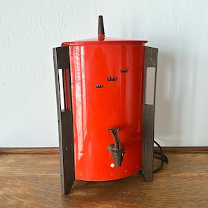 以下が含まれることがあります： ダークブラウンのハンドルとアクセントが付いた、ヴィンテージの赤い電気コーヒーパーコレーター。 パーコレーターは注ぎ口のある円筒形で、濃い茶色の木製パネルに挟まれています。 3つの黒い王冠のデザインが前面にあります。