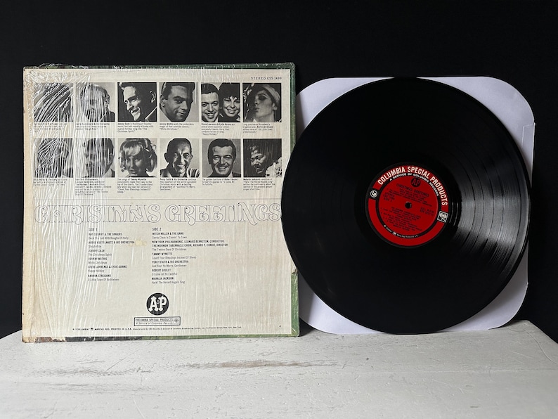May include: A vintage vinyl record album cover with a photo collage of people smiling. The album title is "Christmas Greetings" and the record label is "Columbia Special Products".
