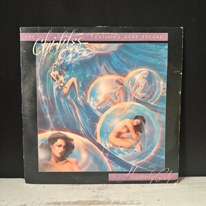 以下が含まれることがあります： 「The Chi-Lites Featuring Gene Record」のアルバムカバー。シュールなイラストが特徴です。青と白の背景に、透明な球体の中に裸の人物が描かれています。「Heavenly Lady」のタイトルが下にあります。