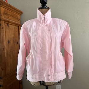 May include: A pale pink jacket with a high collar, button fastening, and front pockets. The jacket has a ribbed hem and cuffs. The jacket is displayed on a mannequin. The jacket is a vintage style.