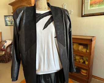 May include: A black leather jacket with a suede collar and a white t-shirt underneath. The jacket has a unique design with a black fabric panel on the front.