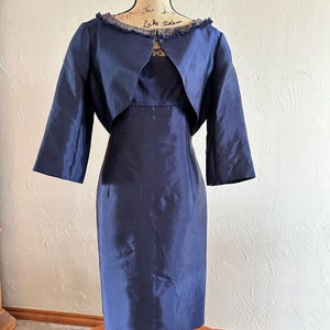 May include: A navy blue dress and matching bolero jacket set. The dress is a sheath style, and the jacket has three-quarter sleeves and a fringed neckline. The set is displayed on a mannequin.