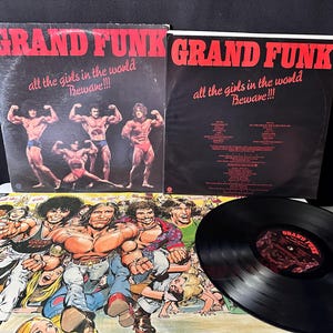 May include: Two Grand Funk Railroad vinyl record covers titled All the Girls in the World Beware!!!, one featuring four muscular men and the other a tracklist, alongside a colorful illustrated inner sleeve and a black vinyl record disc.
