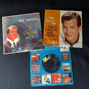 Könnte beinhalten: Drei Vintage-Schallplatten im Format 45 U/min von Pat Boone. Die erste Schallplatte trägt den Titel "A Closer Walk with Thee". Die zweite Schallplatte trägt den Titel "'Twixt Twelve and Twenty". Die dritte Schallplatte ist eine Dot Records 45 U/min Schallplatte mit einem schwarzen Label und dem Titel "Exodus".